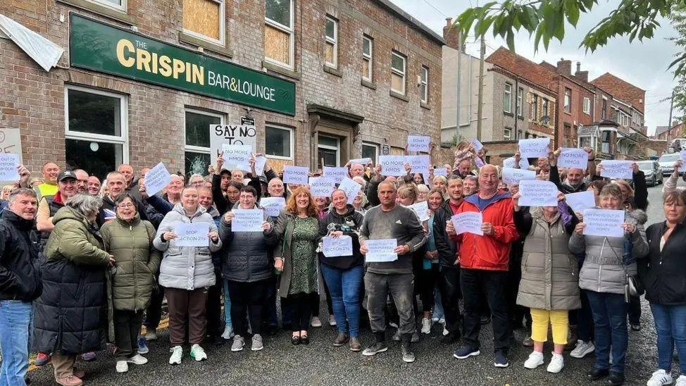 Protesters outside of the Crispin Arms in Wigna holding placards 