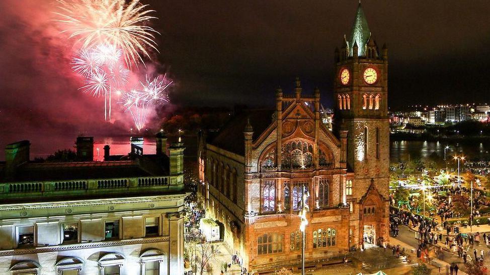 Shows the Guildhall with fireworks on the left and throngs of people on the right.