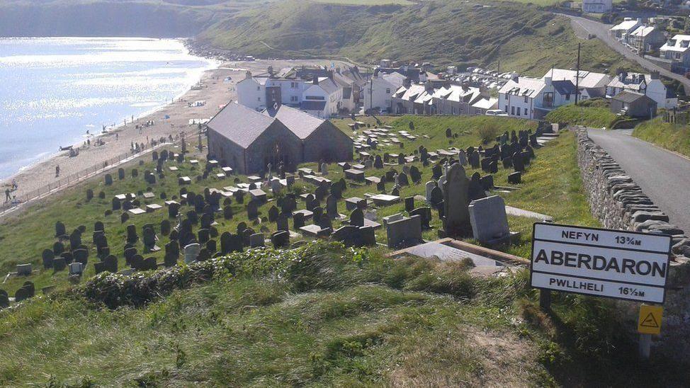 The road into Aberdaron, with a church, houses and the sea in the background, and a sign saying Aberdaron