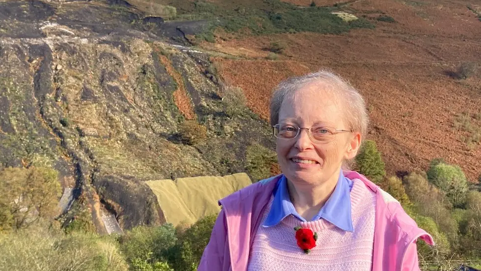 Ann Davies stands in front of the Tylorstown landslide, with scars visible on the mountain behind her