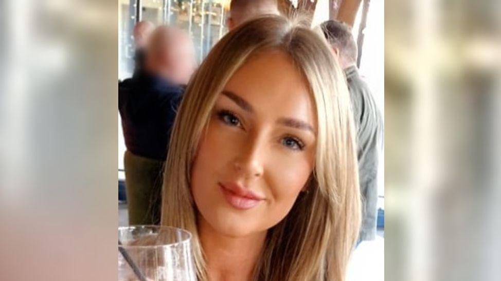 Chloe Lightfoot has blonde hair and is looking at the camera holding a wine glass.