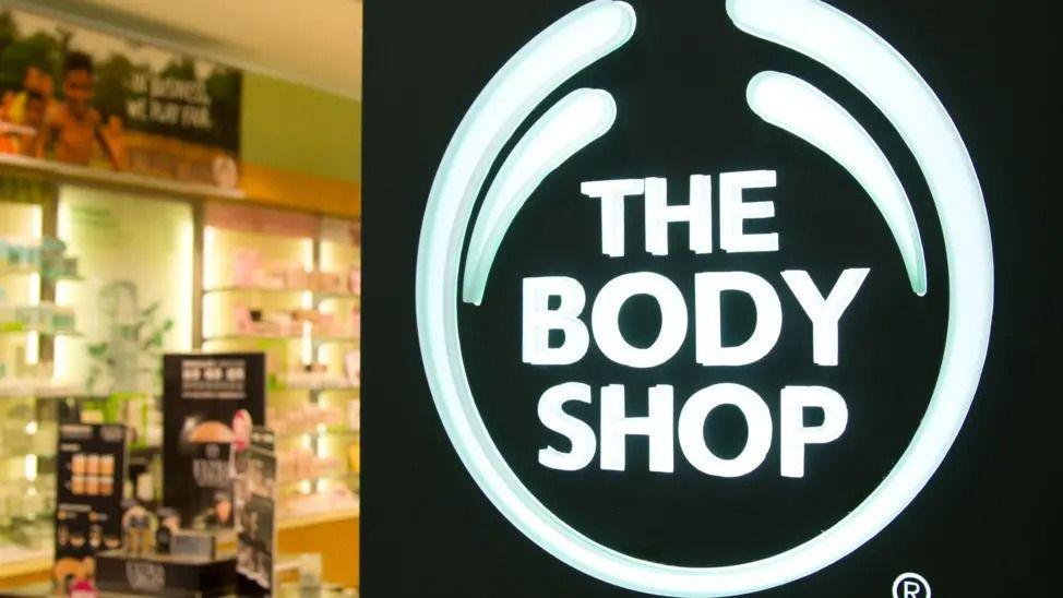 The entry to a Body Shop store, with a large logo in the foreground and cosmetics on a stand in the background