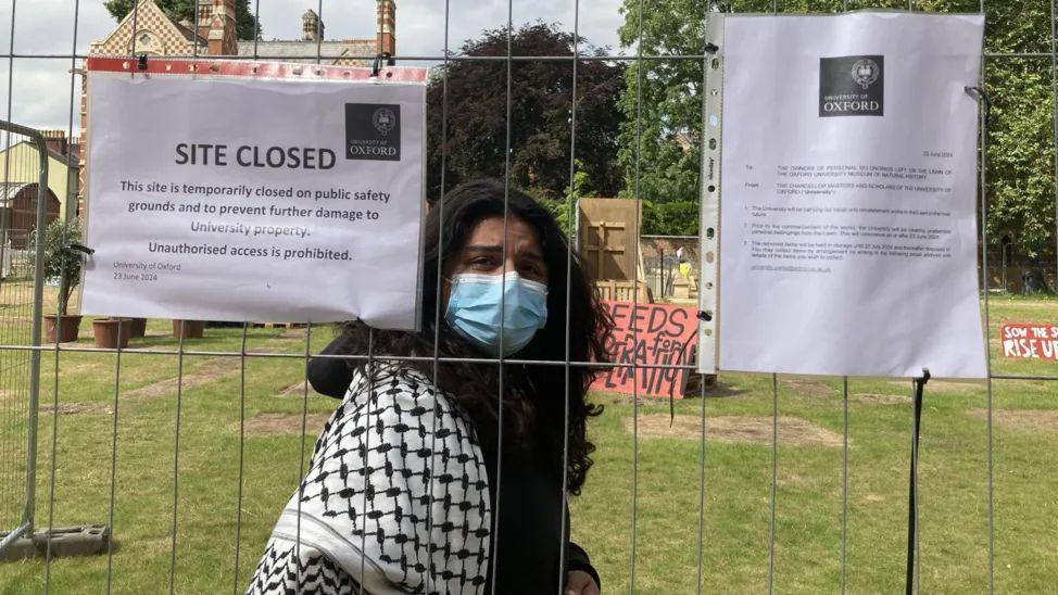 Protester, with surgical mask on, behind metal fencing