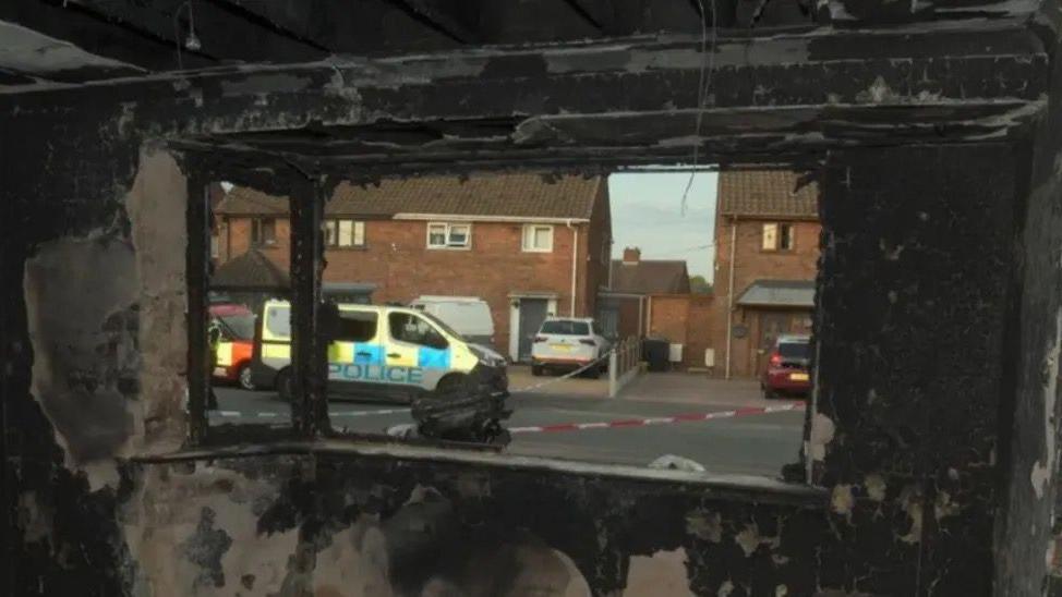 The inside of a home charred by smoke. On the road outside is a police car and cordon 