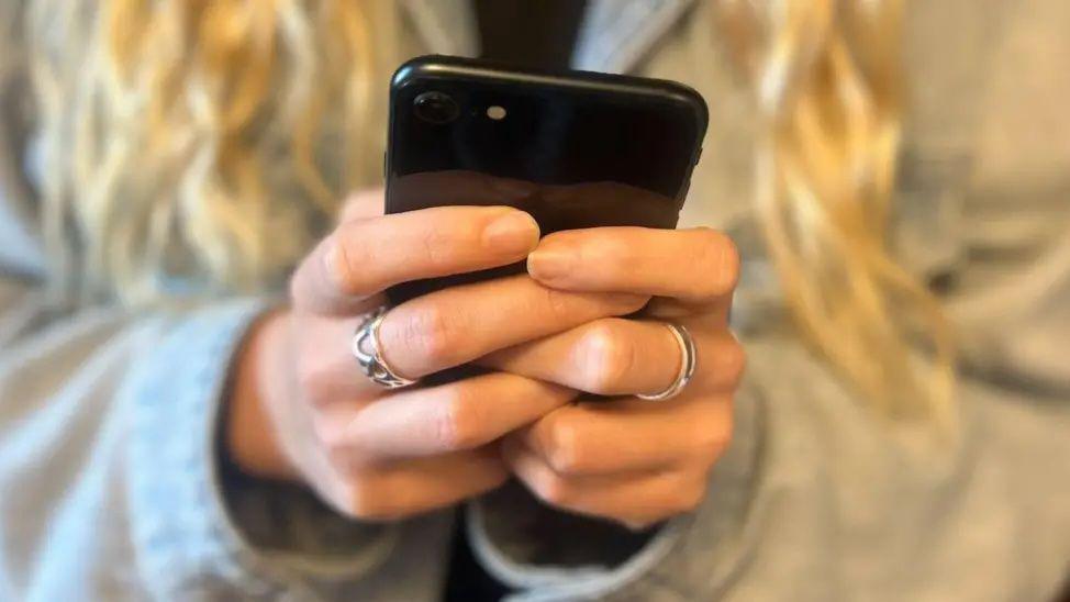 A closeup of a woman's hands wrapped around a black mobile phone handset.