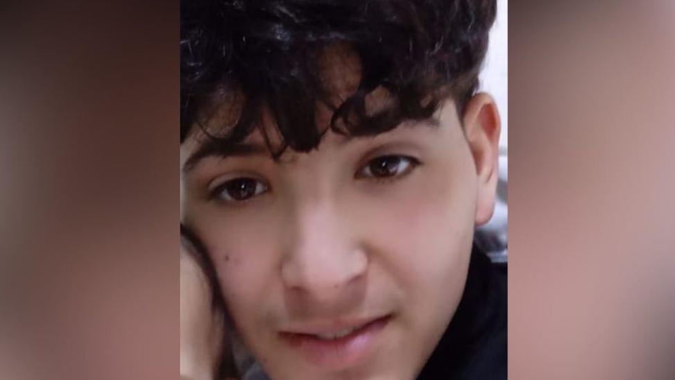A teenage boy with a thick black fringe. His face is resting against what appears to be the side of a baby's head.