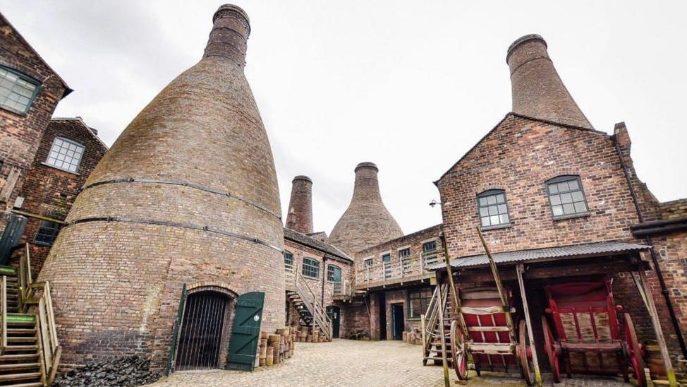 A courtyard of a former pottery, now a heritage site. Brick buildings and four bottle ovens surround the courtyard.