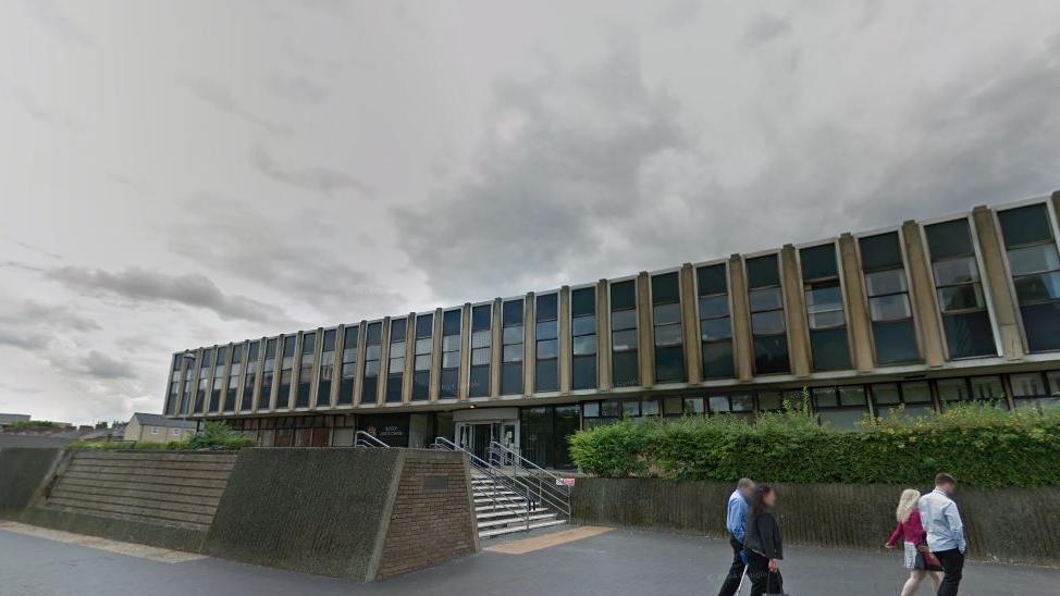 A general view of Teesside Magistrates' Court. A long, two-storey glass and concrete building with hedges in front and wide, concrete steps leading to a large entrance area. 