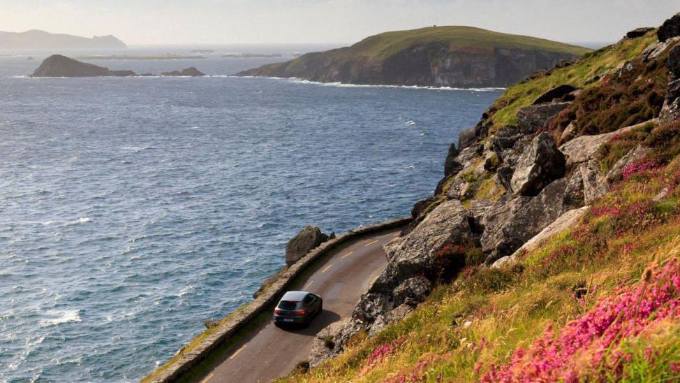 A car being driven along a coastal road in Kinsale, County Cork, a cliff edge is on one of its sides, the sea on the other.