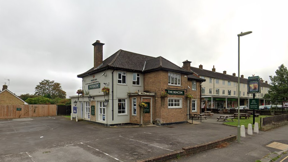 A screenshot from Google street view of a redbrick building with a sign outside saying "The Beacon". The pub's car park is empty and it's a cloudy, overcast day.