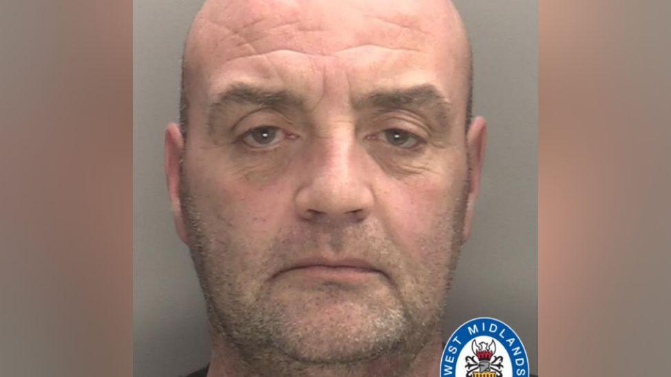 A police mugshot shows a man with a shaved head and stubble. There is a West Midlands Police logo in the bottom right of the image.