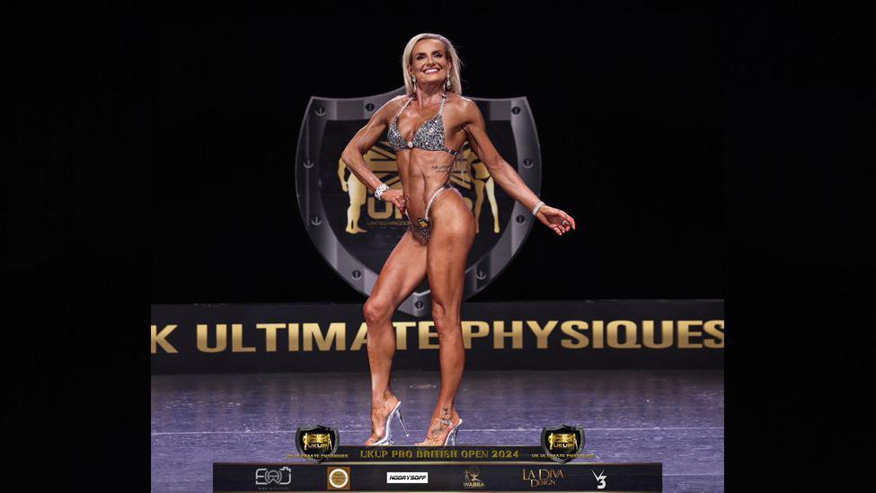 Jane posing on stage at a previous competition