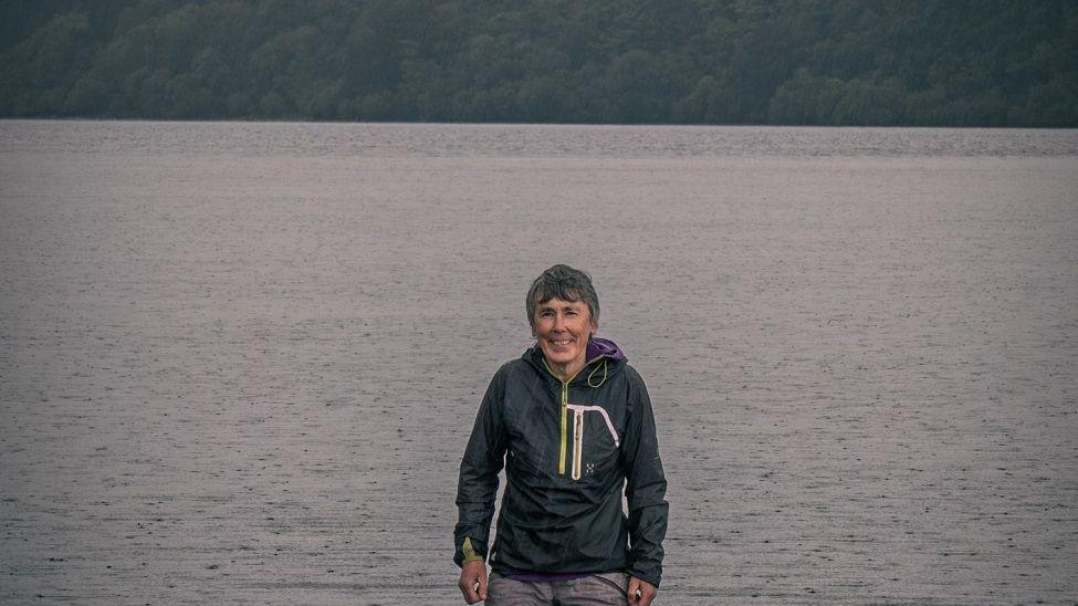 A woman with cropped grey hair standing in front of a lake.