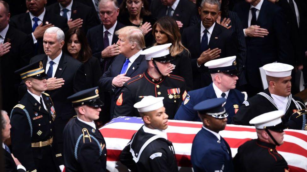 Coffin carrying George HW Bush is carried past Mike Pence, Donald Trump, Melania Trump and Barack Obama as they each hold their right hand against their chest as a mark of respect