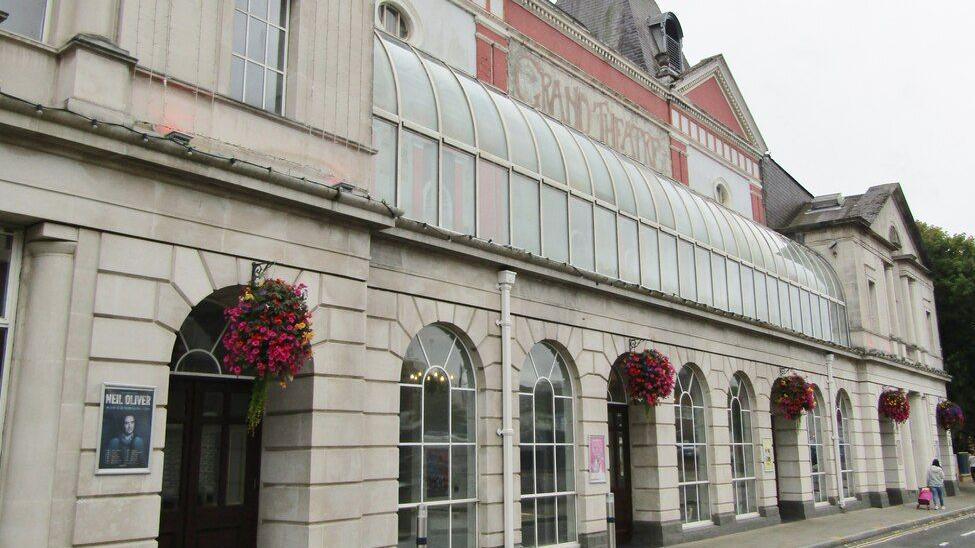 The outside of a theatre with arch windows and the lettering "Grand theatre" at the top.