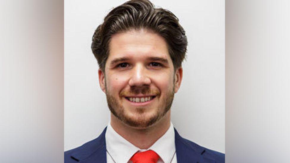 Councillor Kieren Spencer with brown hair, brown eyes and brown beard wearing a red tie and blue blazer smiling.