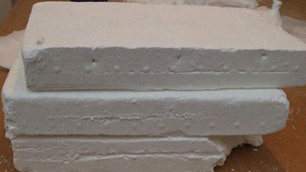 Three rectangular blocks of white cocaine, piled up one on top of the other. They are resting on a wooden table. 