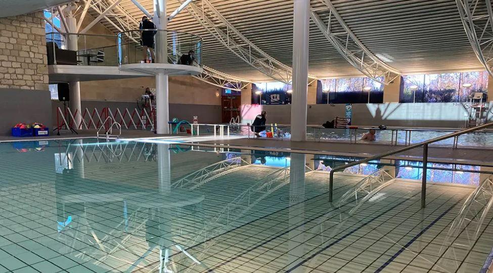 Tadcaster Community Swimming Pool. A large empty pool is in the foreground, with people swimming in a pool next door while a lifeguard looks on.