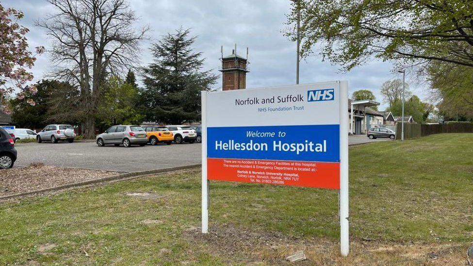 Hospital sign for Hellesdon Hospital, with parked cars and buildings in the background.