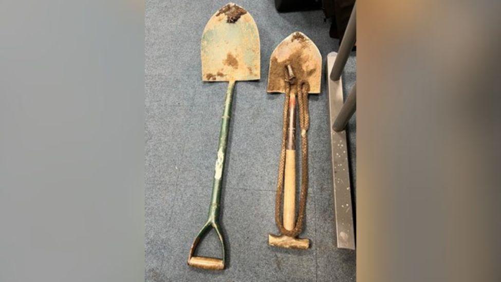 Two large spades covered in mud are laid out on a carpeted floor