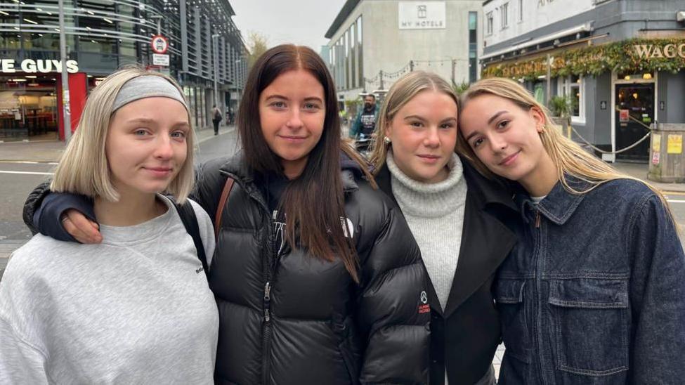 Mid shot of four young female students standing on a Brighton street looking to camera. From left to right - From left: Maddie Bunting, Lauren Hart, Millie Winchester, Blyth Eling, all students from the University of Brighton