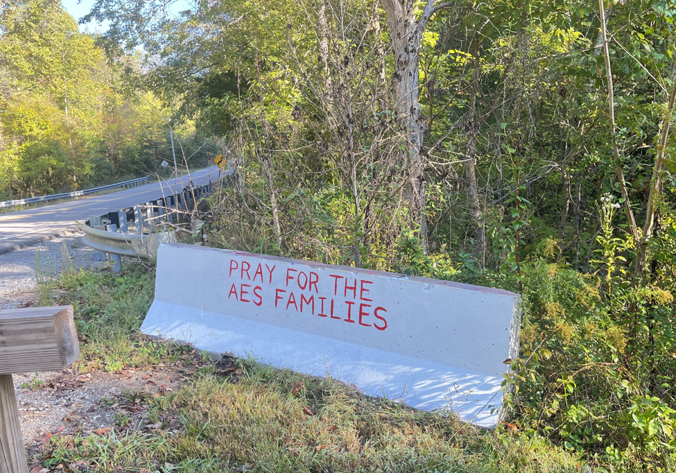 A concrete barrier on the side of a road reads "Pray for AES families".