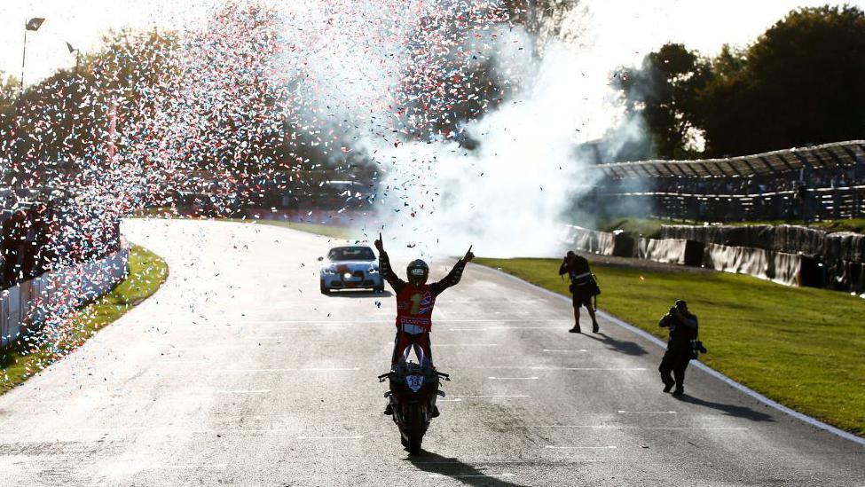 Tommy Bidewell holds his arms in the air as confetti goes off behind him as he crosses the line at Brands Hatch to be crowned champion