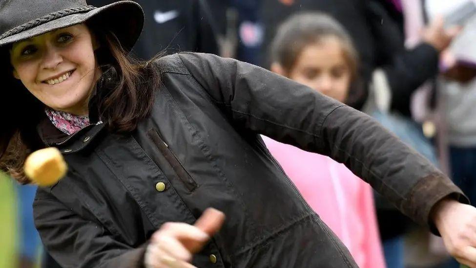 A woman in a wax jacket and hat throwing a Dorset Knob.