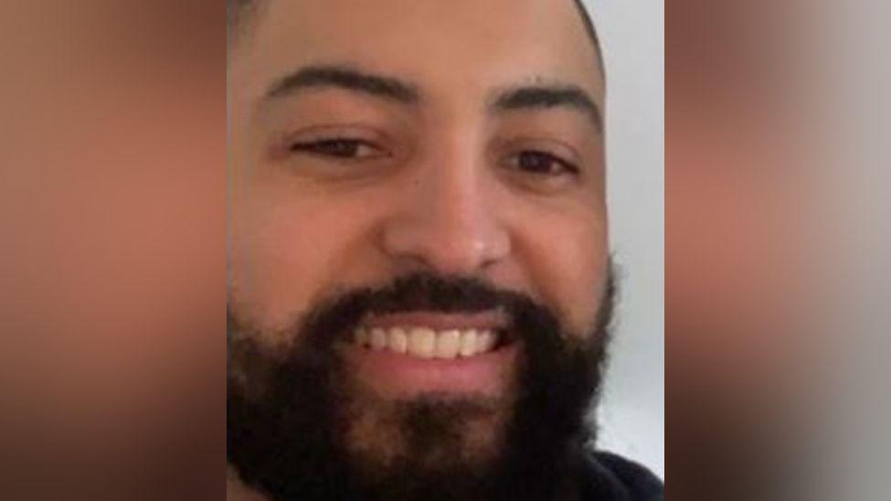 A close-up photo of a man with a black beard and close-cut black hair.