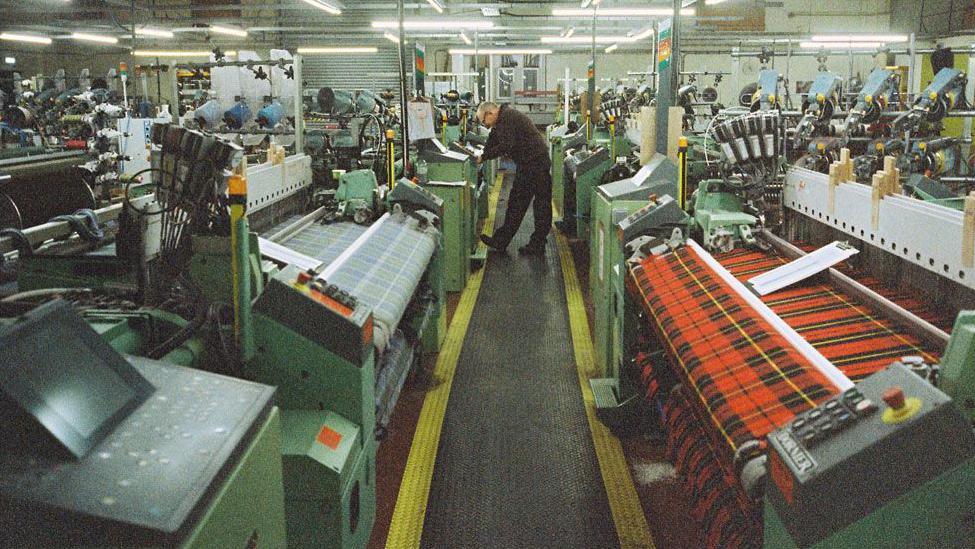 A man bends over a machine at the centre of a Borders textile factory