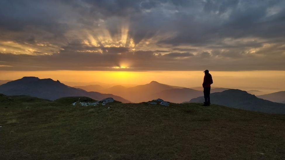 A hillwalker standing looking at the sunrise over Ben Lomond