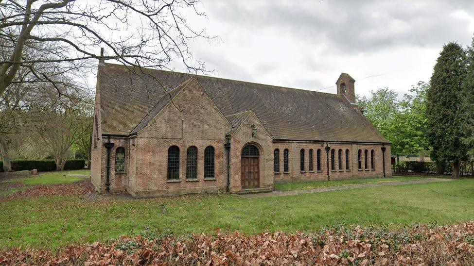 A single storey church building with a grassy lawn and trees.