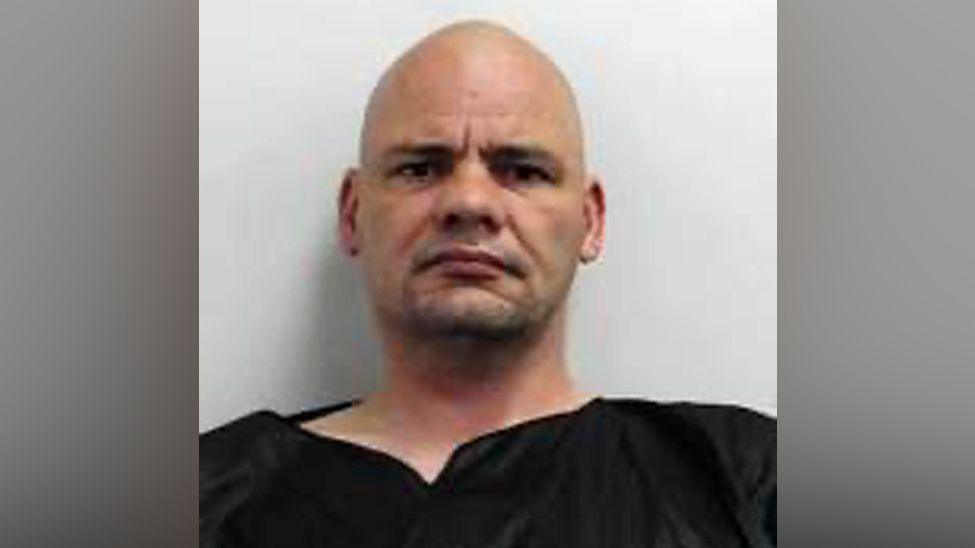 Police mug shot of Wayne Phillipson - a bald headed man wearing a black top