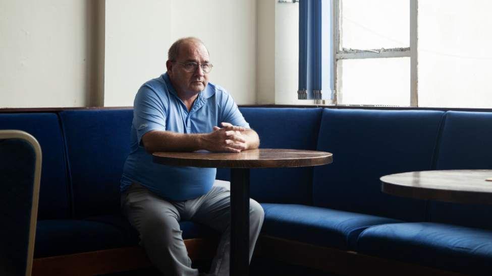 A man sits alone at a table inside Tata Steel's sports and social club room