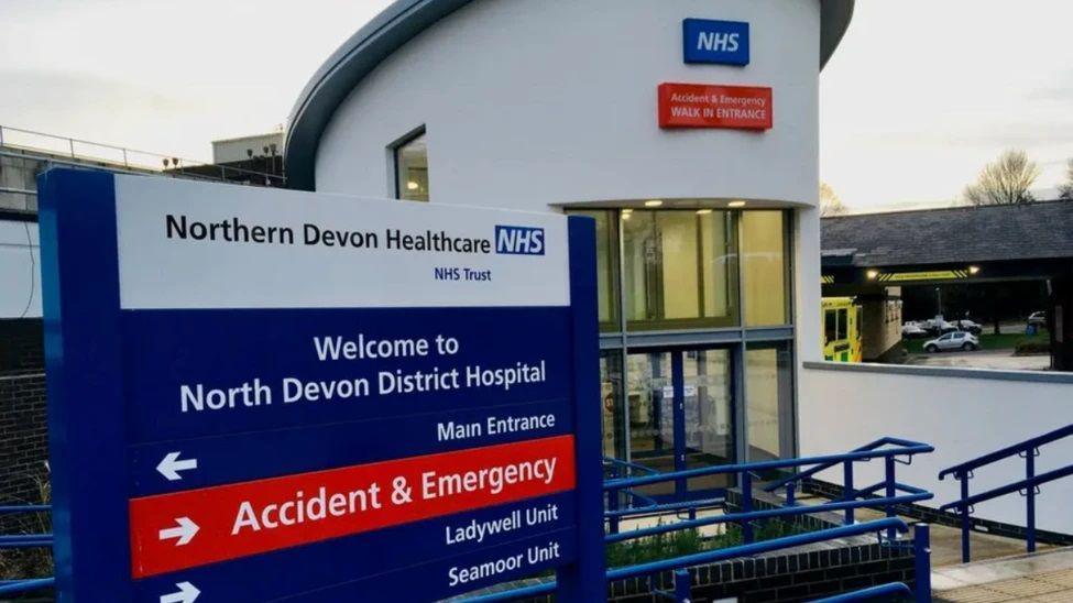 A signpost headed with 'Northern Devon Healthcare NHS Trust' and reading 'Welcome to North Devon District Hospital'. Under that are arrows pointing to the main entrance, accident and emergency, Ladywell unit and Seamoor unit. 