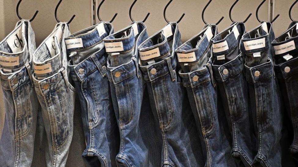 Calvin Klein jeans of different styles hung up in a row on pegs