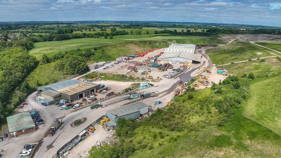 An aerial view of Newton Ayclifffe quarry, surrounded by green fields, with numerous buildings separated by roads and car parks.