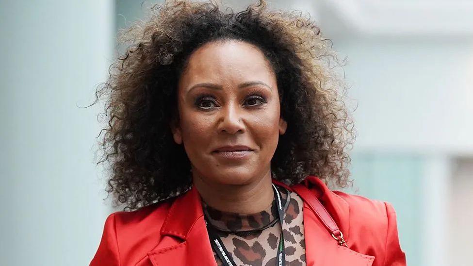 Close up of Mel B smiling and wearing a leopard print under a red jacket