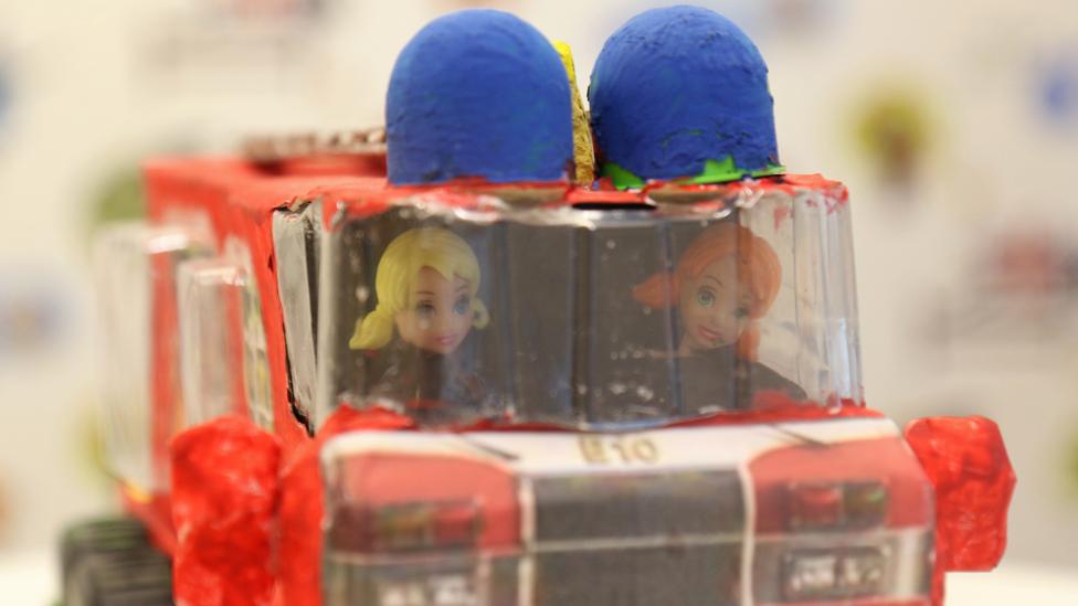 A close-up of the two dolls sat in the fire engine cab.