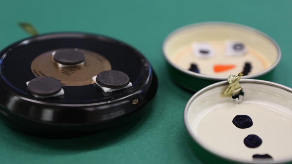 The back of one of the lids, showing the three magnets. Another snowman on the right, with the method of fixing the two lids together visible.