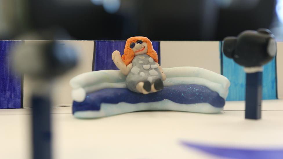 A close-up of the plasticine Lindsey on the BP sofa, with two plasticine cameras pointed at her.