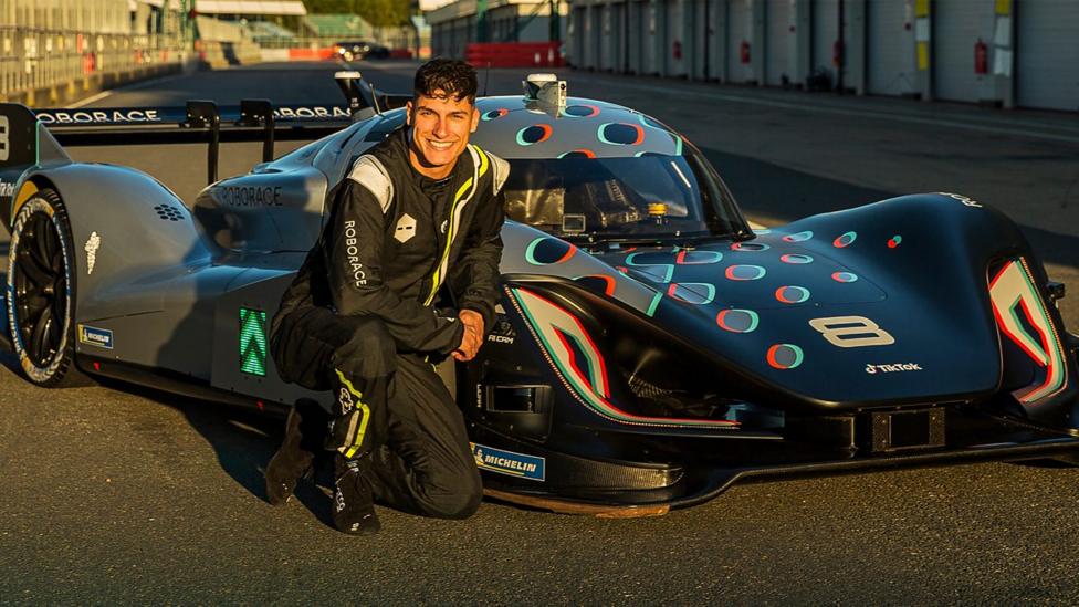 Richie crouched next to a Roborace self-driving car, sat on a racetrack.