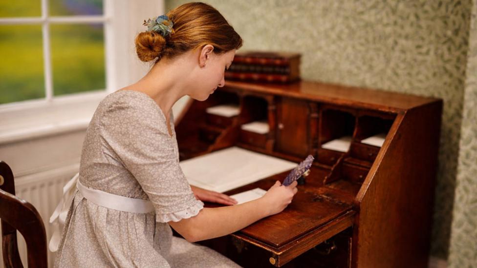 lady_dressed_in_period_costume_leaning_over_writing_desk.