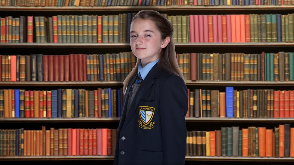 Cassie from So Awkward stands smugly in a library.