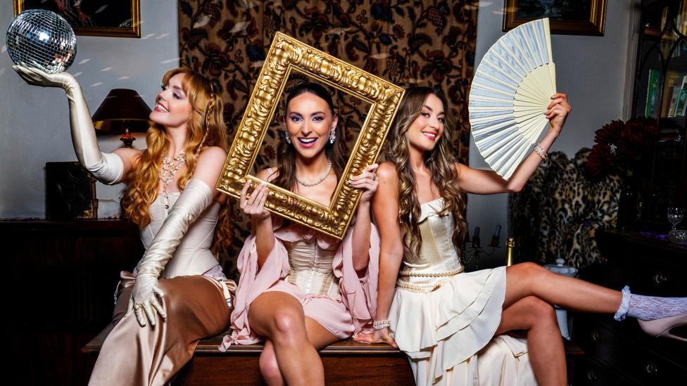 Remember Monday, a girl band, they are posing on a sofa with props including a picture frame, a hand fan and a disco ball.