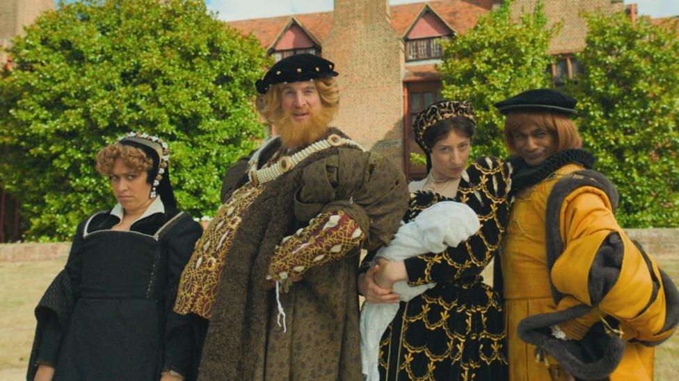 Image of a man dressed as a king surrounded by two women dressed as princesses and a man dressed as a prince in the style of the Tudors.