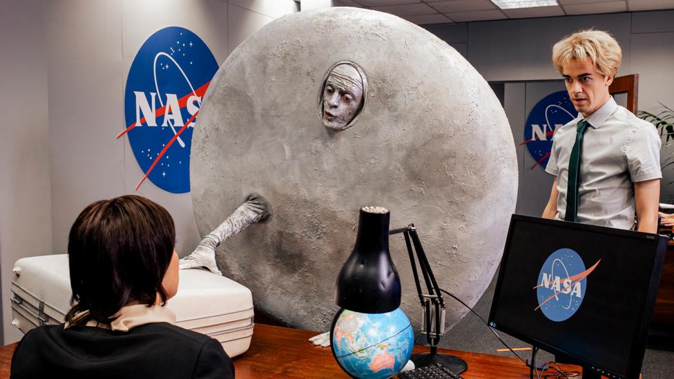 Image of a man dressed like the moon in front of the Nasa logo.