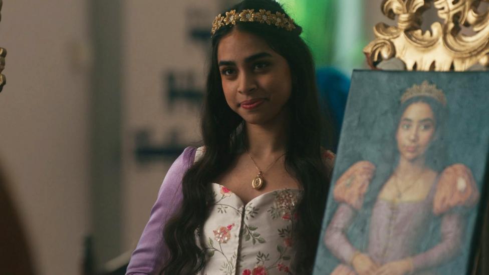 Image of a girl dressed in Tudor outfit posing next to a painting of herself.
