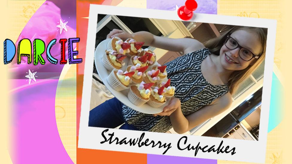 A girl called Darcie holds up a plateful of strawberry and marshmallow cupcakes.