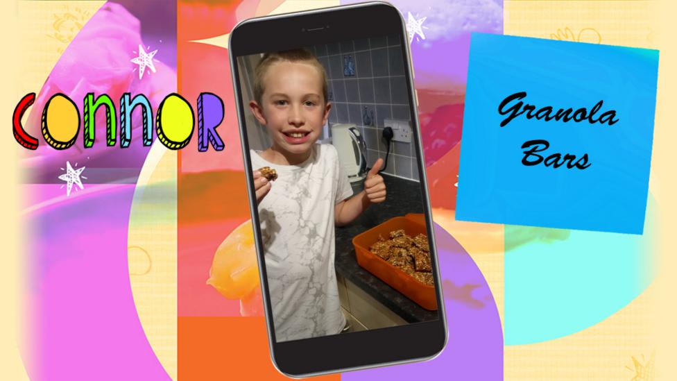 A little boy (Connor) holding a granola boy next to a plastic box of granola, smiling and proud of himself.